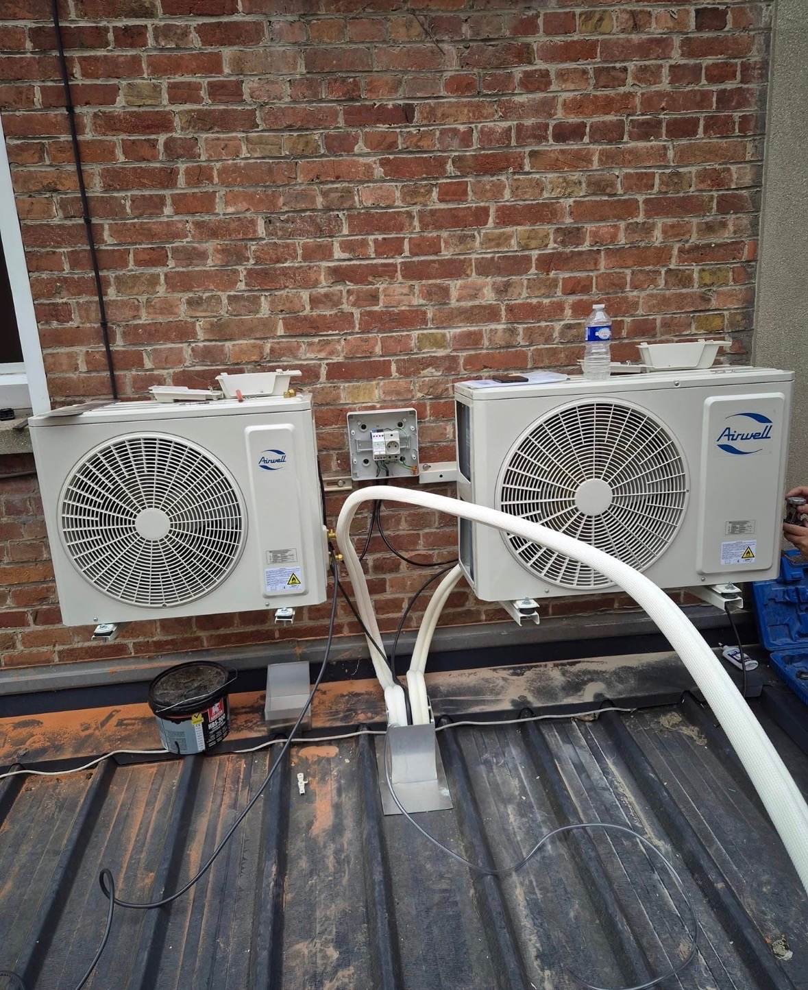 Deux groupes extérieurs de climatisation Airwell posés en bi-split sur un mur de brique par L.I.J Chauffage, près de Monchecourt.