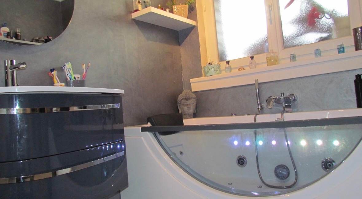 Baignoire balnéo à éclairage LED devant un mur en béton ciré, rénovation de salle de bain réalisée par L.I.J Chauffage près de Monchecourt.