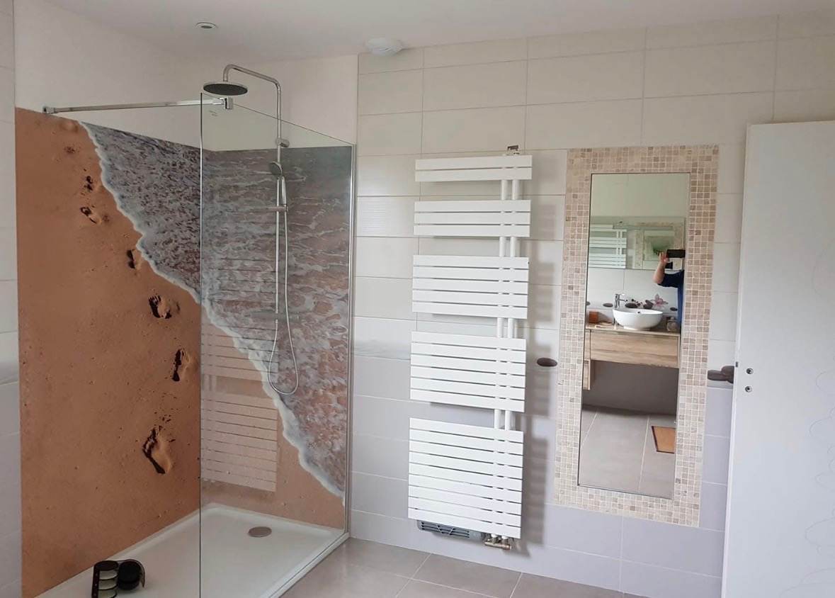 Salle de bain rénovée par L.I.J Chauffage à Monchecourt : douche à l’italienne avec paroi vitrée, panneau mural décor plage et sèche-serviettes design.